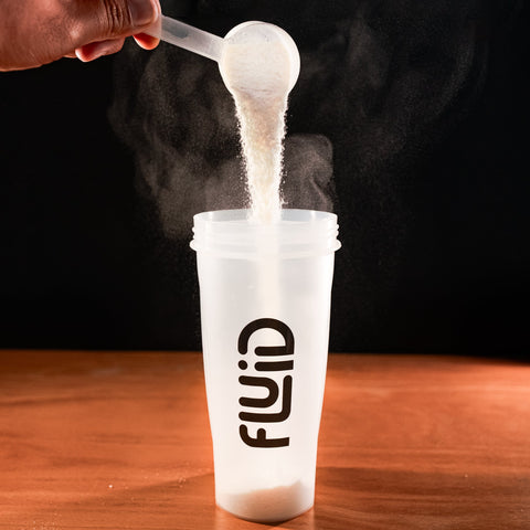 Person pouring powder into a 'Fluid' container on a wooden surface with a dark background