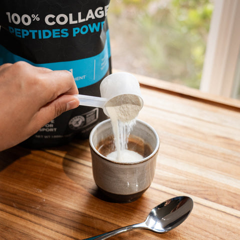 Person adding Fluid 100% Collagen Peptides to a cup of coffee on a wooden table.