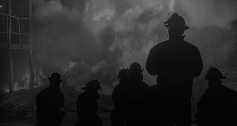 Silhouettes of firefighters against a dark background with smoke and fire.