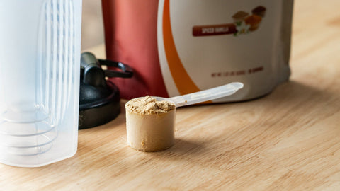 Powdered supplement in a scoop with a container in the background on a wooden surface