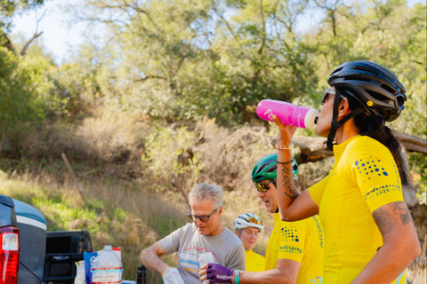 Two cyclists in yellow jerseys preparing for a ride outdoors with trees in the background.