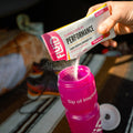 Person pouring Fluid Performance Raspberry Lemonade 50g Carb packet into a pink sports bottle.