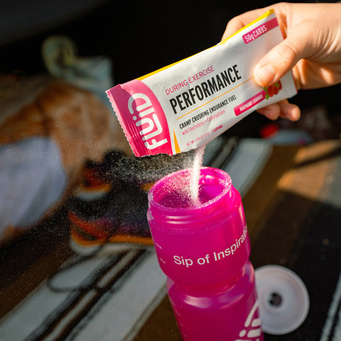 Person pouring Fluid Performance Raspberry Lemonade 50g Carb packet into a pink sports bottle.