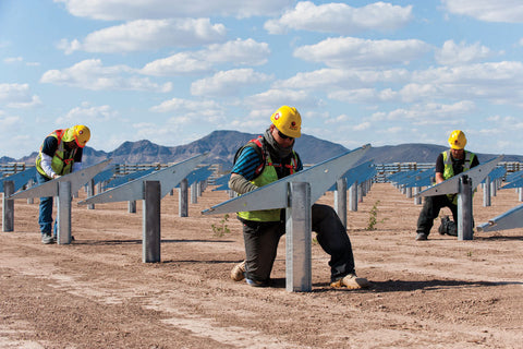 Three workers installing solar panels on a desert landscape with mountains in the background.
